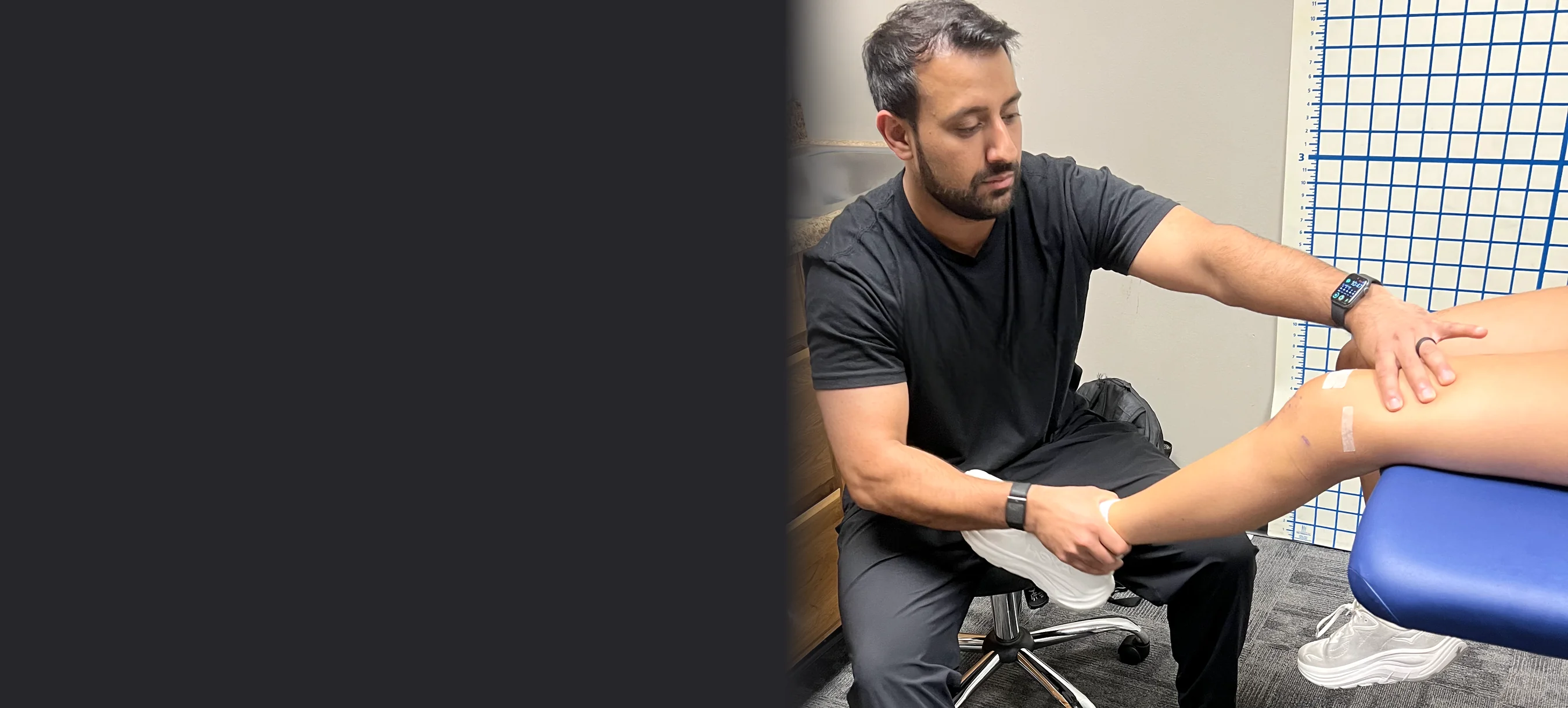 TJ examining a seated patient’s knee beside the grid wall