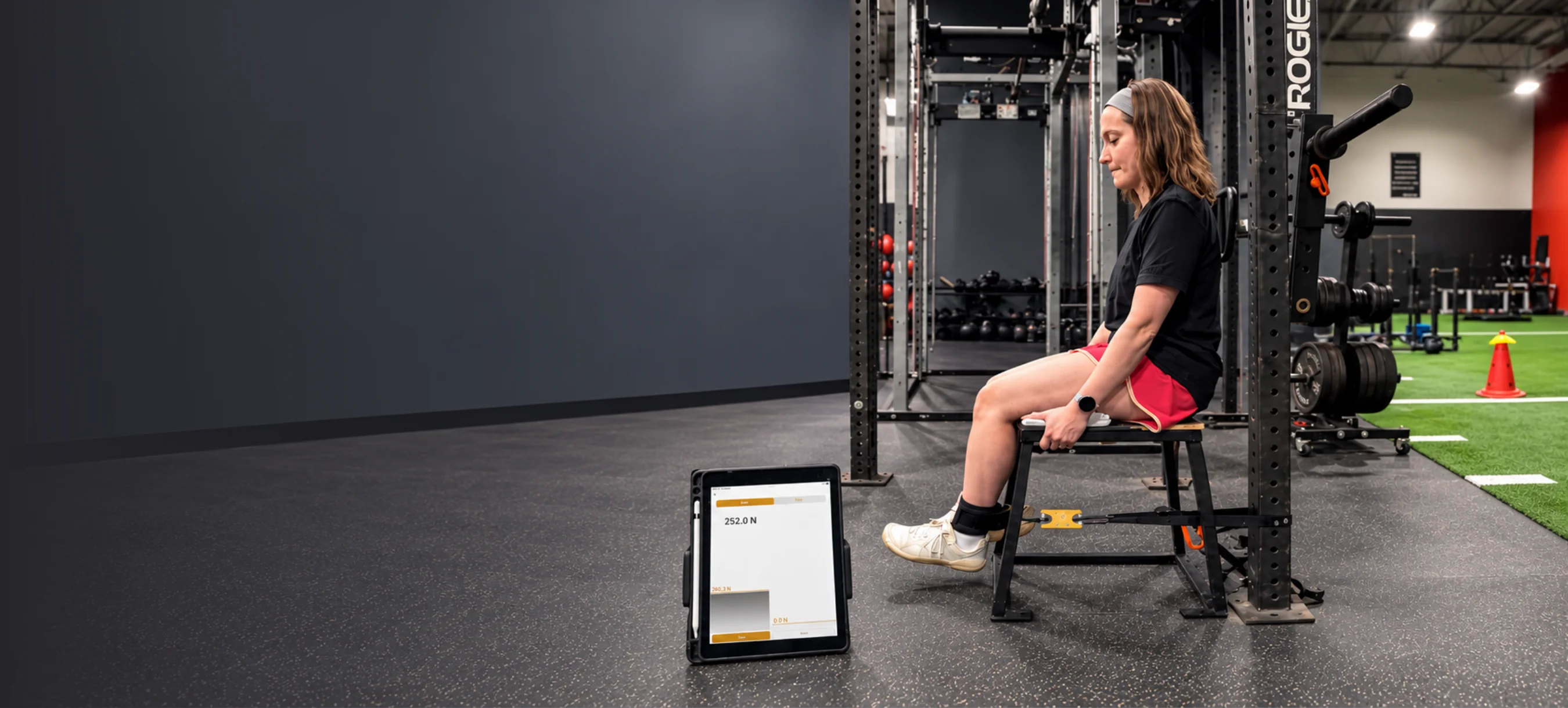 An athlete performing a knee strength test with the result on a tablet
