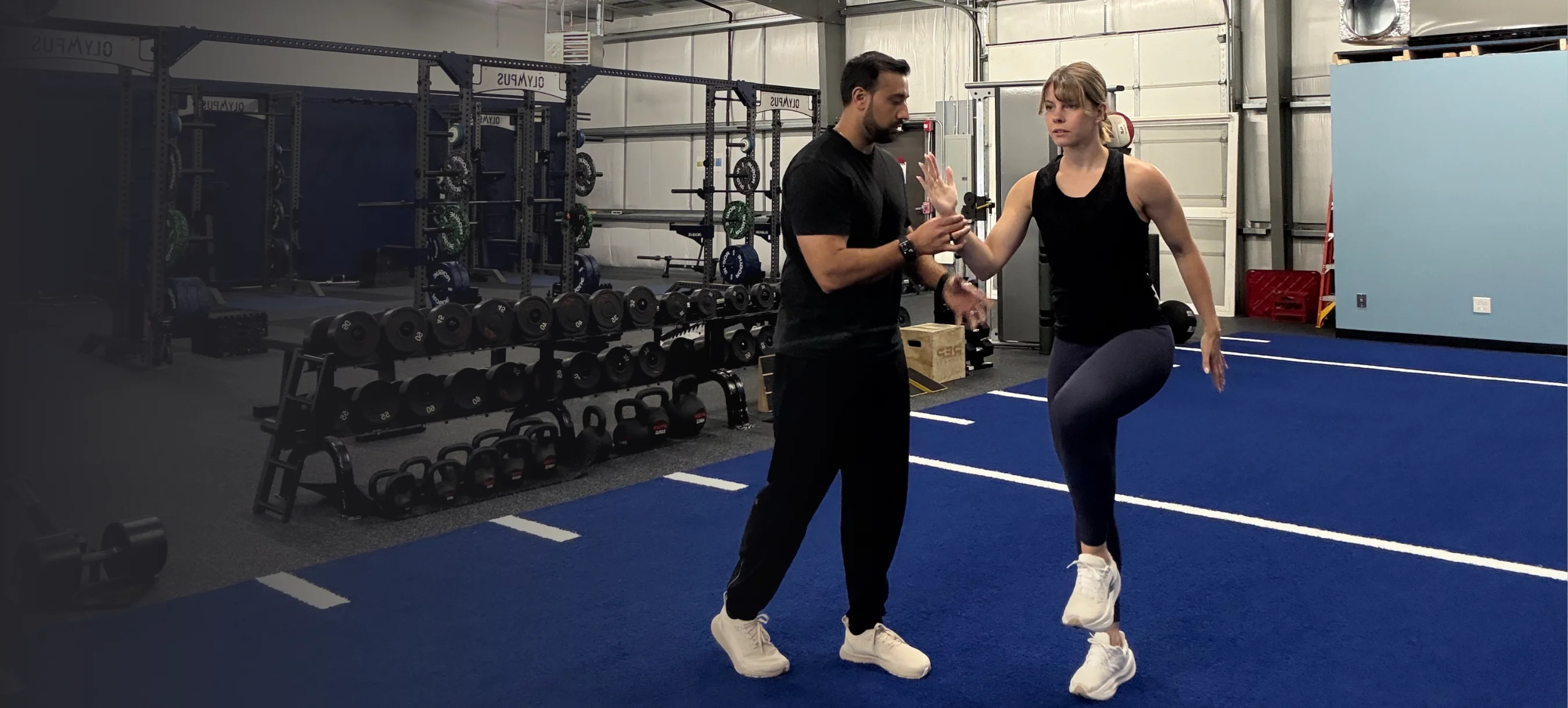 TJ guiding an athlete through a single-leg drill on the gym turf