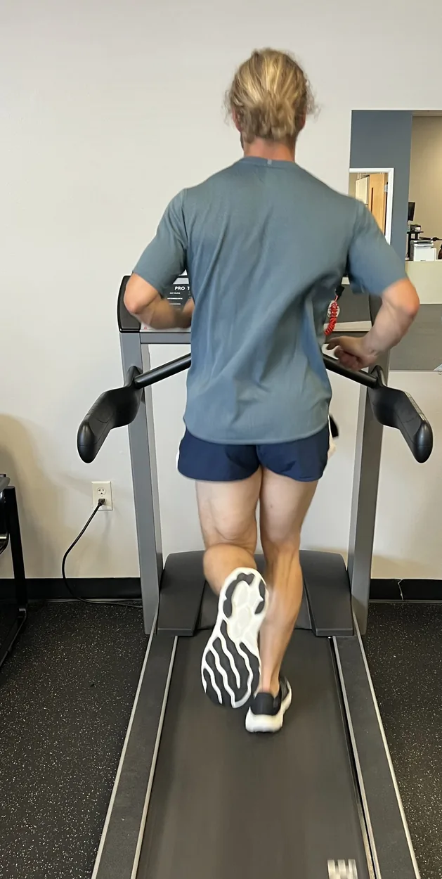 A runner on the treadmill seen from behind, with gait analysis lines over the pelvis, trunk and stance leg